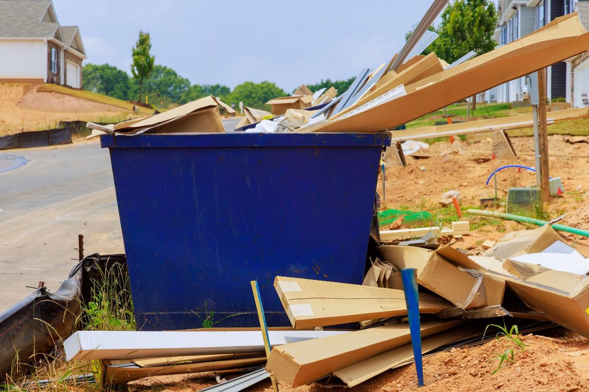Drywall sheets and offcuts piled beside a construction bin during a renovation